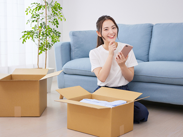 スマホを持って荷造りをする女性